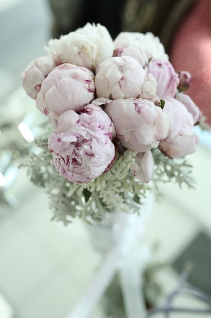 A bouquet of soft pink peonies with delicate, ruffled petals, arranged in a clear glass vase. The peonies are fresh, with slightly open blooms revealing intricate layers of petals. The bouquet is plac