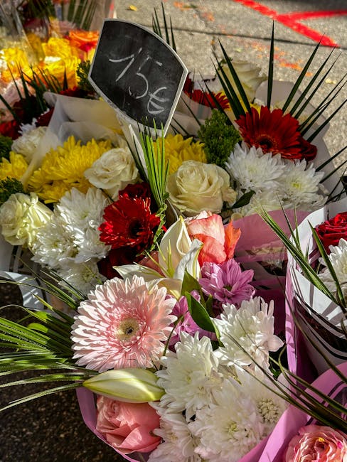 A vibrant display of fresh floral bouquets featuring a mix of white, yellow, pink, red, and purple flowers including roses, gerbera daisies, chrysanthemums, and lilies, with greenery accents and long